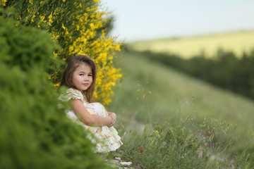 Child sitting in nature in a meadow with green grass.