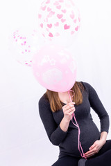 Fototapeta premium Young pregnant woman sitting with balloons - Gender Reveal - It's a Girl !