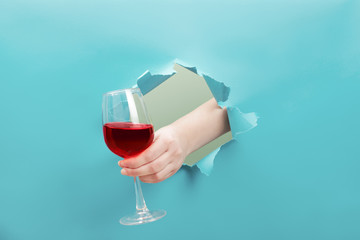 Hand holds a glass of red wine through a torn hole. Event celebration concept.