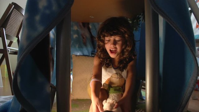 A pretty child girl is playing with jumping acrobat plush puppets in her hidden lair under table at home  FDV
