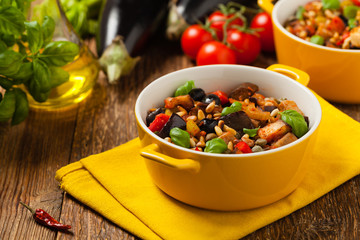 Traditional Italian caponata, served with croutons in a yellow, sunny pot. Decorated with basil and pine nuts.
