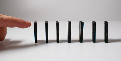 Black pieces of dominoes with white dots, arranged by a curve, waiting to be pushed down by a human finger