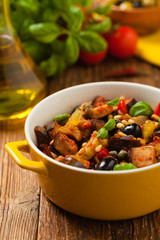 Traditional Italian caponata, served with croutons in a yellow, sunny pot. Decorated with basil and pine nuts.