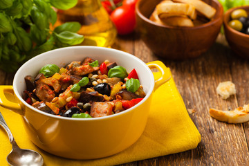Traditional Italian caponata, served with croutons in a yellow, sunny pot. Decorated with basil and pine nuts.