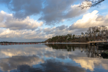 Fototapeta na wymiar Panoramic view of Baltic Sea bay in spring. Landscape with beautiful clouds reflect on water. Horizon, skyline. Islands with pines and houses. Modern residence on the rocky shore. Archipelago, Sweden.