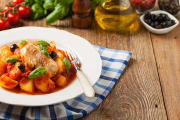 Traditionally prepared cod in Spanish. Served in tomato sauce with boiled potatoes, olivki and basil. Front view.