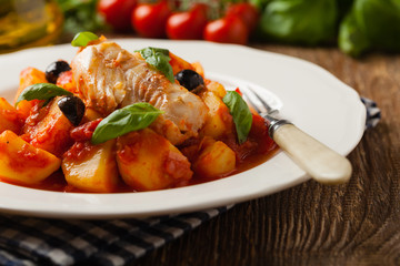 Traditionally prepared cod in Spanish. Served in tomato sauce with boiled potatoes, olivki and basil. Front view.