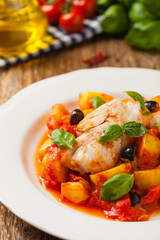 Traditionally prepared cod in Spanish. Served in tomato sauce with boiled potatoes, olivki and basil. Front view.