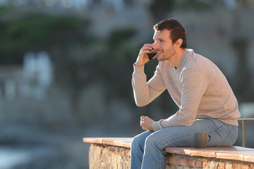 Fototapeta premium Happy man calls on mobile phone sitting on a wall