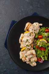 Fried cod served with mushroom sauce and salads. Portion on a black plate. Dark background.