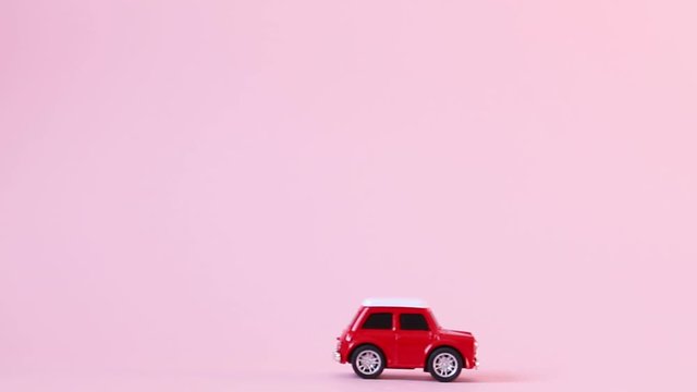 Red toy model car with a golden pattern egg on a pink background. Happy easter concept. Gift delivery.