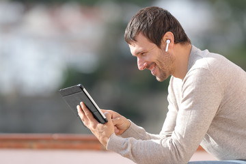 Obraz premium Profile of happy man watching media with tablet and earbuds