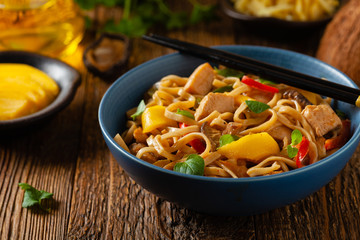 Fried chicken with mango and coconut milk with noodles. Prepared in a wok. Front view. Served in a blue bowl.