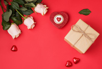 Valentine's Day gifts on a red background next to burning candles, heart-shaped sweets, white roses. copy space.