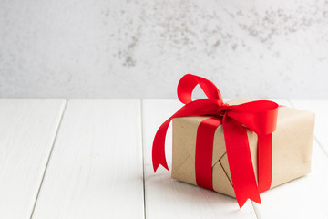 gift box with red ribbon on white wooden table with copy space for your greeting.