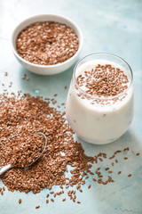 Bowl with flax seeds and glass of yogurt on color background