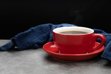 Red cup of coffee with smoke and blue fabric on cement background.