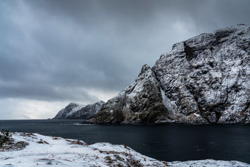 Nordic winter landscape with a fjord, snowy mountain and outstanding clouds above. Lofoten islands, Norway.