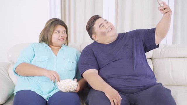 Happy overweight couple taking selfie photo with a mobile phone in the living room at home. Shot in 4k resolution