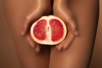 cropped view of woman in nylon tights holding grapefruit half isolated on brown
