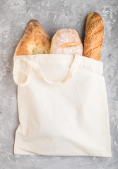 Reusable grocery bag with fresh baked bread on a gray concrete background. top view, copy space.