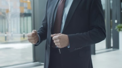 Close-up arc shot of hands and midsection of two anonymous Caucasian and black businessmen in formal suits and ties greeting each other in hallway of office building, shaking hands and talking