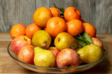 Naklejka na ściany i meble Apples, pears and tangerines in a plate on a wooden background.