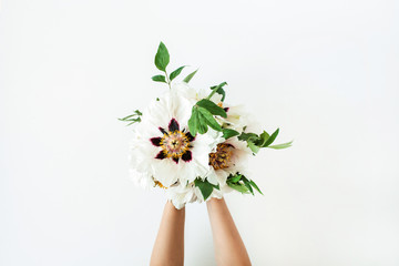 Woman hands holding white peonies flowers on white background. Flat lay, top view.