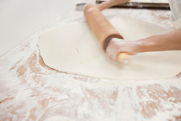 Close-up of male baker's hands with rolling pin on dough in bakery