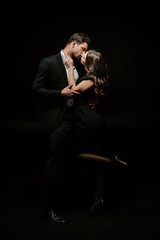 woman kissing handsome man in suit isolated on black
