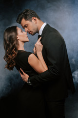 side view of man hugging attractive woman on black with smoke