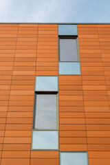 Architecture detail of modern building with orange facade and windows reflecting the sky.