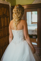 Fototapeta premium Bridesmaid helping slender bride lacing her wedding white dress, buttoning on delicate lace pattern with fluffy skirt on waist. Morning bridal preparation details newlyweds. Wedding day moments, wear.