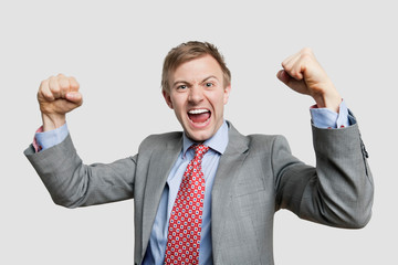 Portrait of young businessman screaming while clenching fist over light gray background