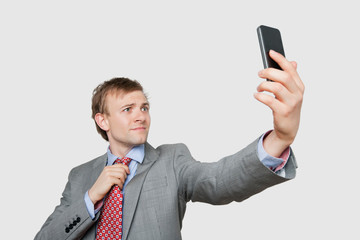 Young businessman taking self photograph while adjusting tie over colored background