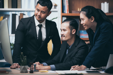 Coworkers looking at a computer and discussing over new business plan. Business team working together on computer in office.
