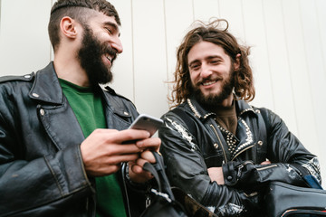 Photo of bearded joyful men bikers using cellphone and smiling