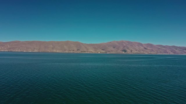 Aerial drone shot pan shot circular of Lake Sevan on background of Mount Ararat. Aerial drone zoom in shot of Lake Sevan under bright blue sky