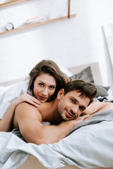 Obraz na płótnie Canvas happy young woman lying on bed with muscular boyfriend