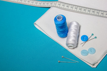 Sewing accessories and fabric on a blue background. Sewing threads, needles, pins, fabric.