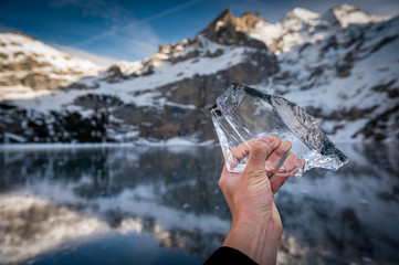 hand holding a beautiful clear chunk of ice on frozen lake Oeschinensee with reflection and Blümlisalp Mountains in Berner Oberland - Powered by Adobe