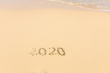 Summer beach holiday 2020 season golden sand - year - decade - new season lettering on the beach with wave and clear blue sea. Numbers 2020 year on the sea shore, message handwritten New Years concept