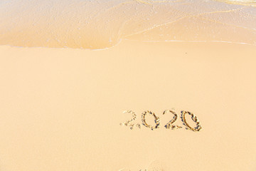 Summer beach holiday 2020 season golden sand - year - decade - new season lettering on the beach with wave and clear blue sea. Numbers 2020 year on the sea shore, message handwritten New Years concept