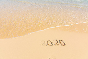 Summer beach holiday 2020 season golden sand - year - decade - new season lettering on the beach with wave and clear blue sea. Numbers 2020 year on the sea shore, message handwritten New Years concept