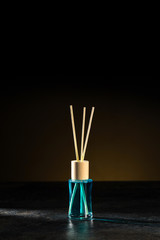 Air freshener, reed diffuser and aromatherapy concept - a bottle of home fragrance standing on a stone countertop on a beautiful dark brown background. Vertical.