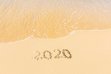 Summer beach holiday 2020 season golden sand - year - decade - new season lettering on the beach with wave and clear blue sea. Numbers 2020 year on the sea shore, message handwritten New Years concept