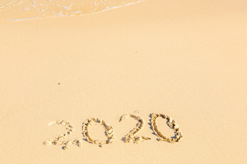 Summer beach holiday 2020 season golden sand - year - decade - new season lettering on the beach with wave and clear blue sea. Numbers 2020 year on the sea shore, message handwritten New Years concept