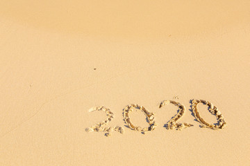 Summer beach holiday 2020 season golden sand - year - decade - new season lettering on the beach with wave and clear blue sea. Numbers 2020 year on the sea shore, message handwritten New Years concept