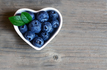 Freshly picked organic blueberries in a white heart shaped bowl on wooden background.Blueberry. Bilberries. Healthy eating,vegan food or diet concept with copy space.Selective focus.