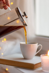 Pouring french press coffee on a windowsill with book and candle